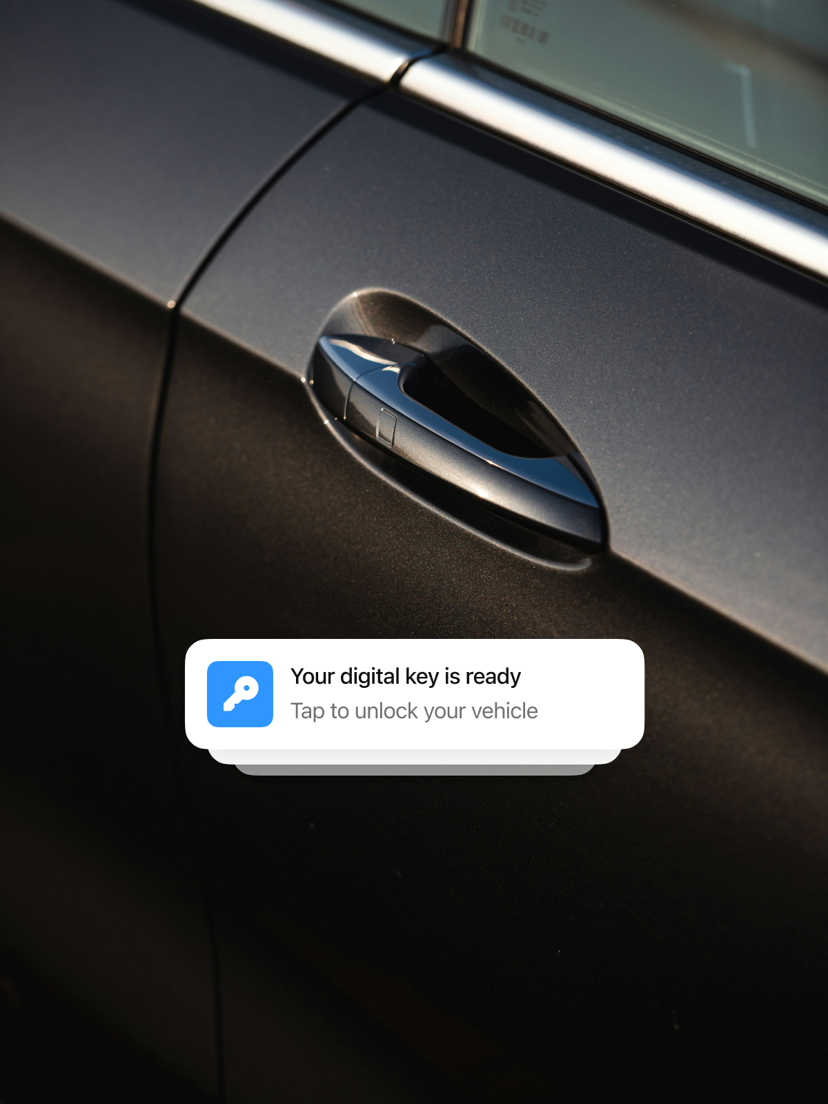 Close-up of a dark-colored car door with a chrome handle, featuring a notification at the bottom that says, 'Your digital key is ready. Tap to unlock your vehicle.'