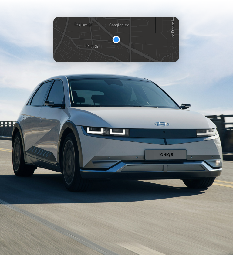 A silver Hyundai Ioniq 5 electric vehicle driving on a road, with a map overlay showing a location marked on it.
