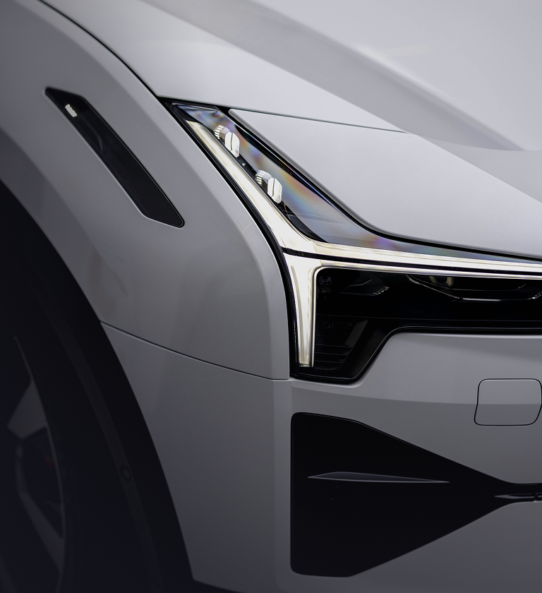 Close-up view of the front headlight and grille of a modern white car, showcasing sleek design elements and chrome accents.